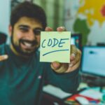 man in grey sweater holding yellow sticky note